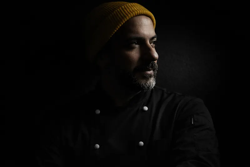 Chef Homero Meyer, de uniforme preto e gorro amarelo.